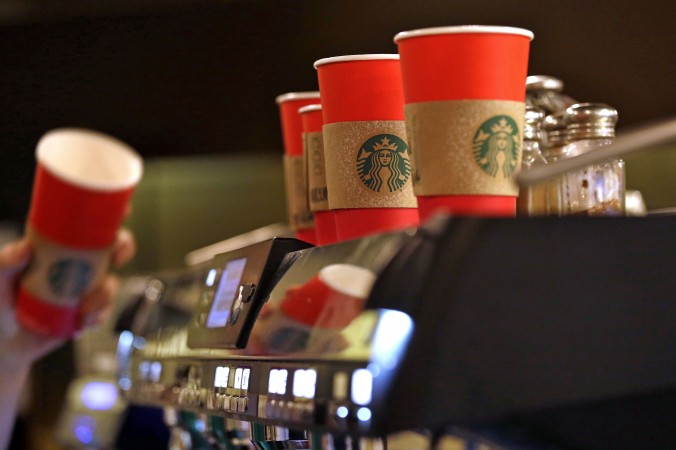 A barista reaches for a red paper cup as more with cardboard liners already attached line the top of an espresso machine at a Starbucks coffee shop in the Pike Place Market Tuesday Nov. 10 2015 in Seattle. It's as red as Santa's suit a poinsettia