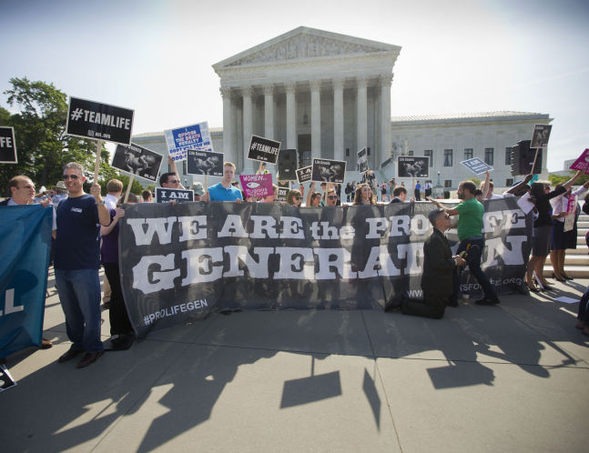 Demonstrators stand on the steps outside the Supreme Court last year as the court was poised to deliver its verdict in a case that weighs the religious rights of employers and the right of women to the birth control of their choice. The Supreme Court is