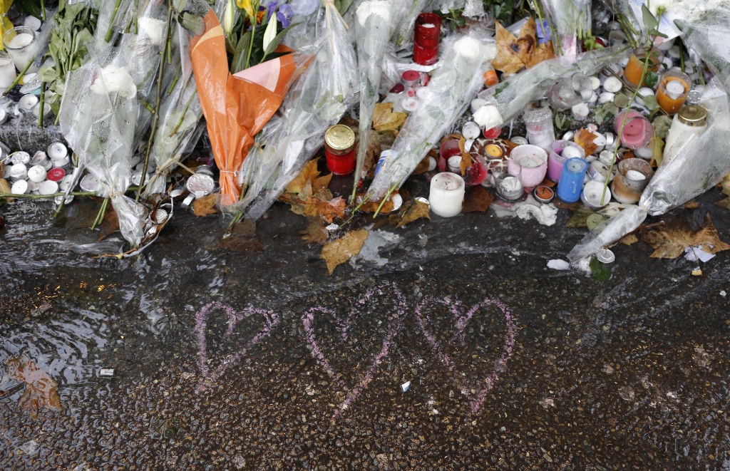 Hearts drawn and flowers lay on the pavement at a bar where an attack took place last week Friday on Friday Nov. 20 2015 in Paris. old rain extinguished the flickering candles and drenched the packets of flowers outside the Paris attacks sites Friday