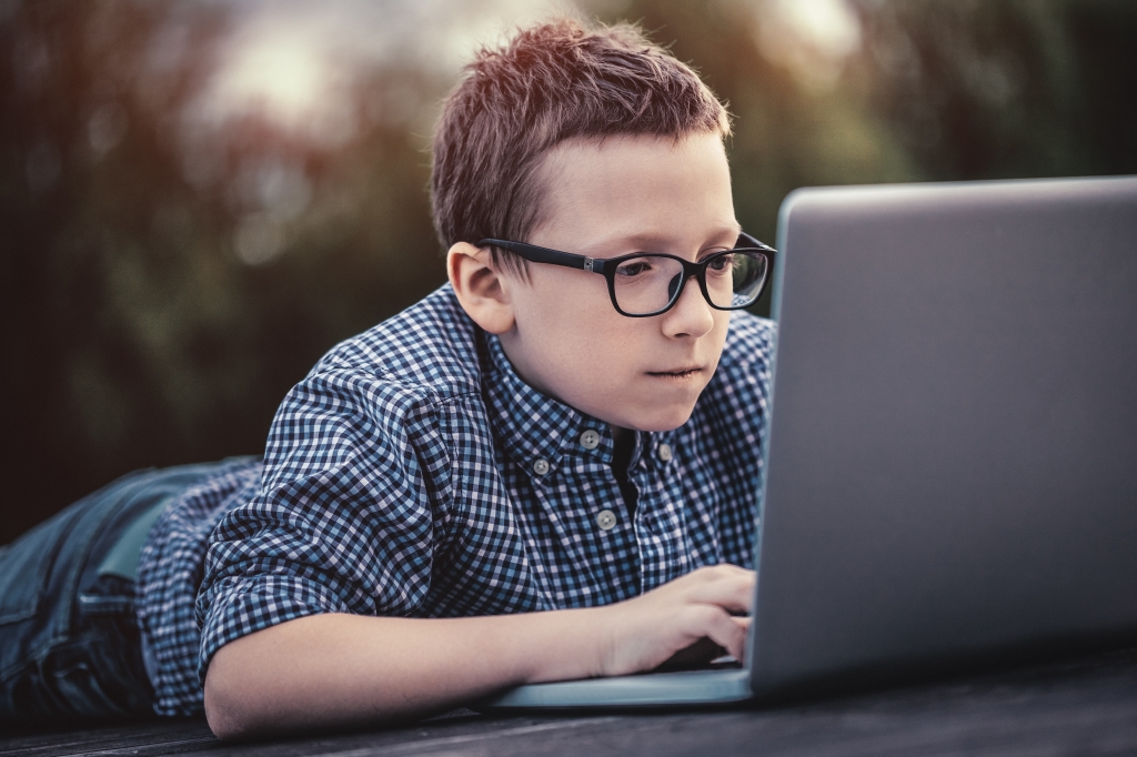 Boy using a laptop lying on wooden pier at sunset