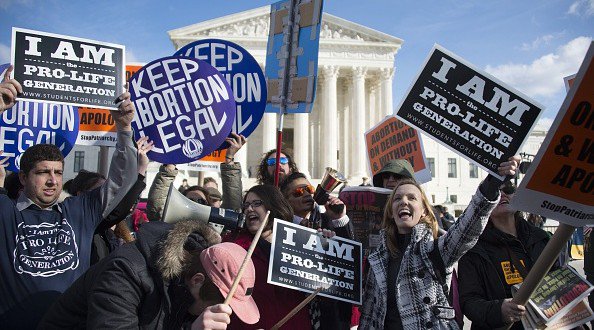 Pro-choice and pro-life activists mingle as they hold up placards and chant in front of the US Supreme Court in Washington DC