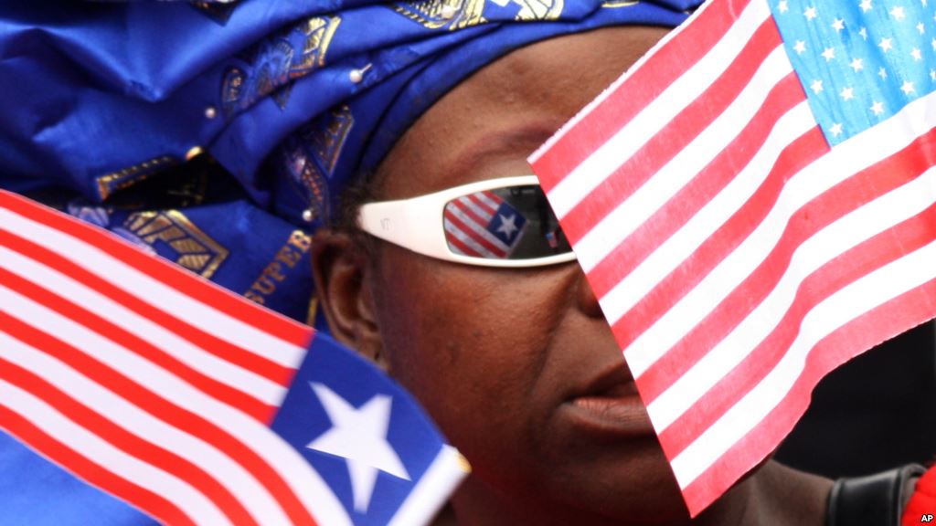 FILE- A market vendor stands among a group of women waving Liberian and American flags to show support for visiting U.S. Secretary of State Hillary Rodham Clinton in Monrovia Liberia. Obama recently lifted US sanctions on Liberia