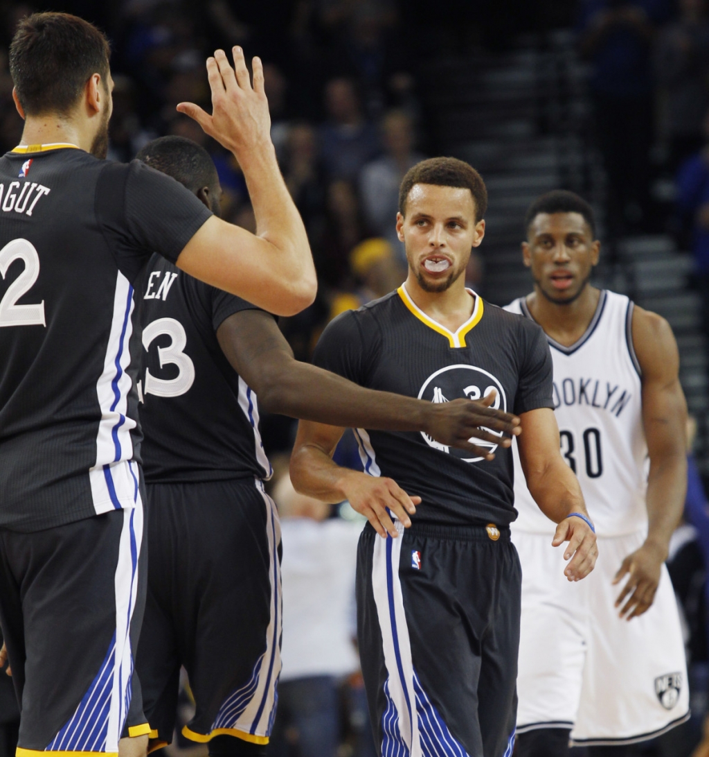 Golden State Warriors&#039 Stephen Curry second from right celebrates with teammates Andrew Bogut left and Draymond Green after Curry sunk a three-pointer during the second half of an NBA basketball game against the Brooklyn Nets Saturday Nov. 14