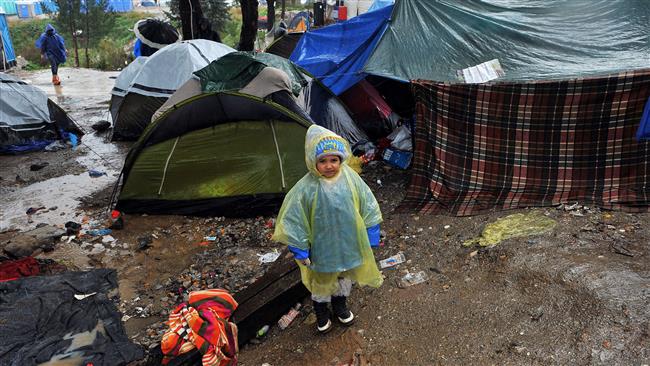 A child in a raincoat stands at a makeshift camp as refugees wait to cross the Greek Macedonian border near Idomeni