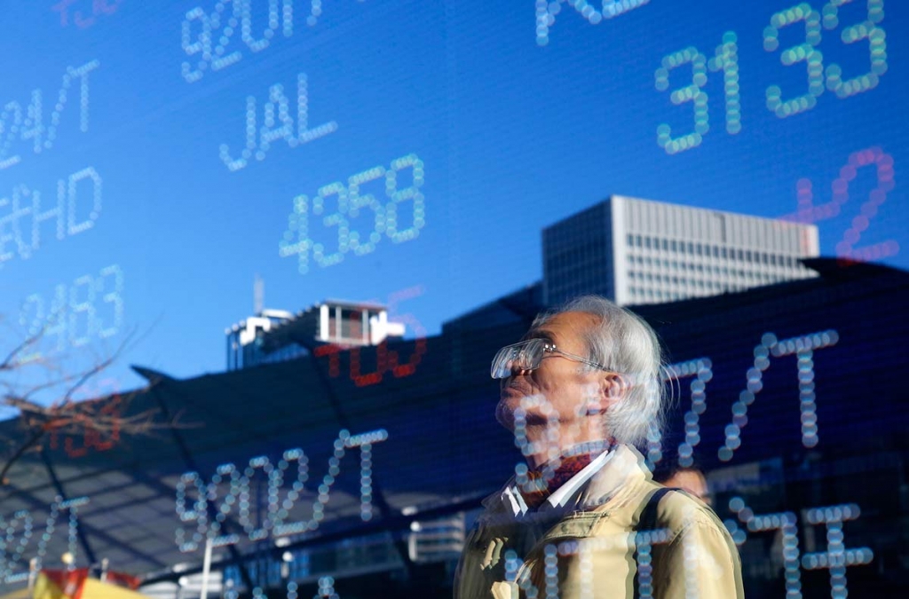 A man is reflected on an electronic stock indicator of a securities firm in Tokyo Tuesday Dec. 29 2015