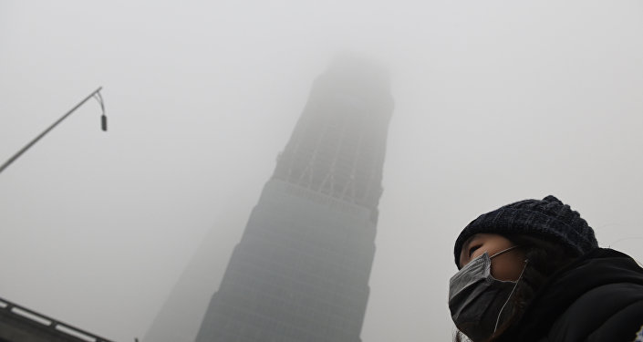 A woman waits for a bus below a skyscraper shrouded in smog on a heavily polluted day in Beijing