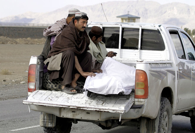 Afghan men move the dead body of a man after clashes between Taliban fighters and Afghan forces in Kandahar Airfield Afghanistan Wednesday Dec. 9 2015. A Taliban assault on an airport in the southern Afghan city of Kandahar that has been underway for