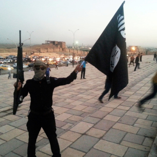 A fighter of the Islamic State of Iraq and the Levant holds an ISIL flag and a weapon on a street in the city of Mosul in this