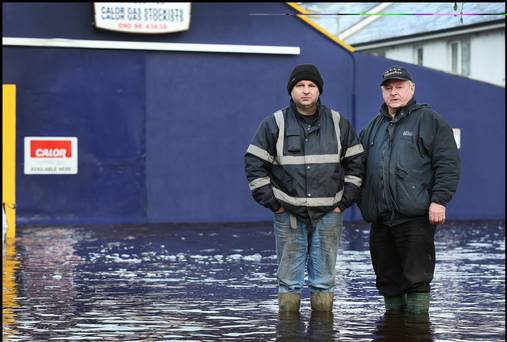 Anthony and Peter Madden from Peter Madden Fuels stand in flood water outside their premises in Ballinasloe yesterday