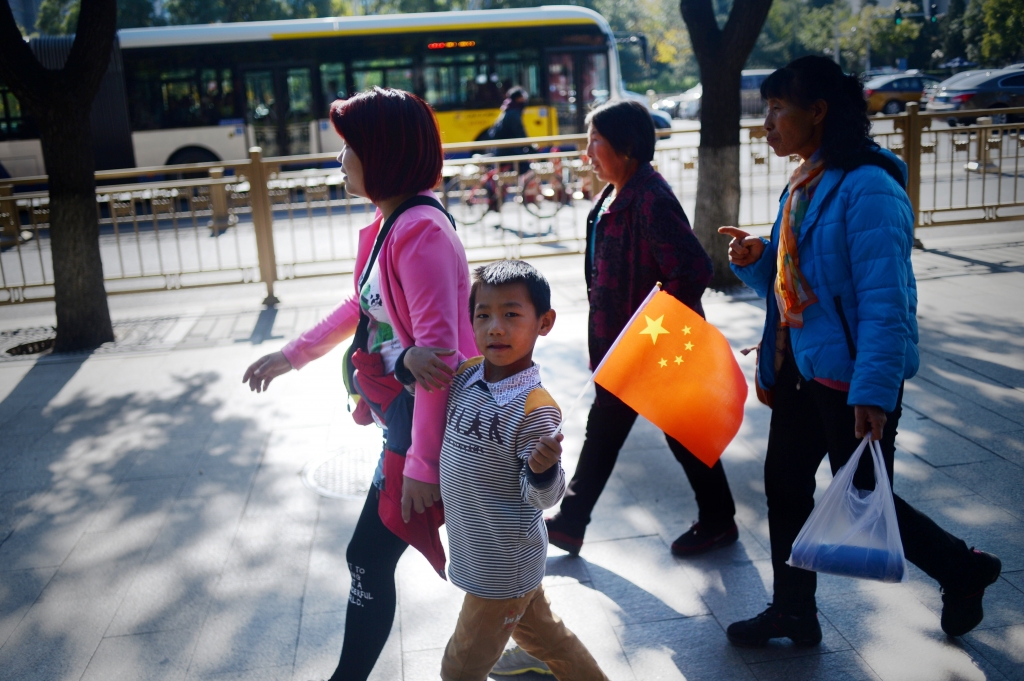 A woman and a child holding up a miniature national flag walk along a road in Beijing on Oct. 31 2015. China announced the end of its hugely controversial one-child policy the day before after decades of strict sometimes brutal enforcement left it with