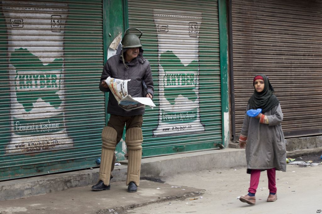 FILE- An Indian policeman reading newspaper watches a Kashmiri girl walk past him during restrictions in Srinagar Indian controlled Kashmir