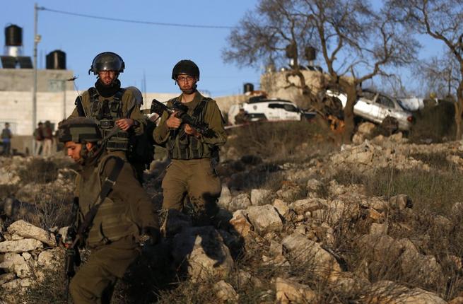 Israeli soldiers walk at the site where a Palestinian driver ran over and injured two Israeli soldiers near the Jewish settlement of Ofra in the Israeli occupied West Bank