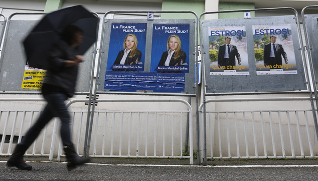 A woman walks past electoral posters of far right National Front party regional leader for southern France Marion Marechal Le Pen left and French right-wi