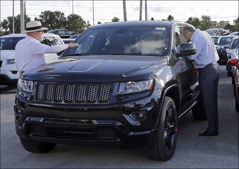 A salesperson Andrew Montalvo left talks to a customer checking out the interior of a 2015 Grand Cherokee Limited in Doral Fla