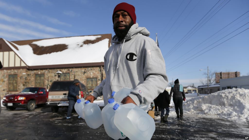 FILE- Lemott Thomas carries free water being distributed at the Lincoln Park United Methodist Church in Flint Mich. Feb. 3 2015. Flint's mayor has declared a state of emergency due to problems with the city's water system caused by using water