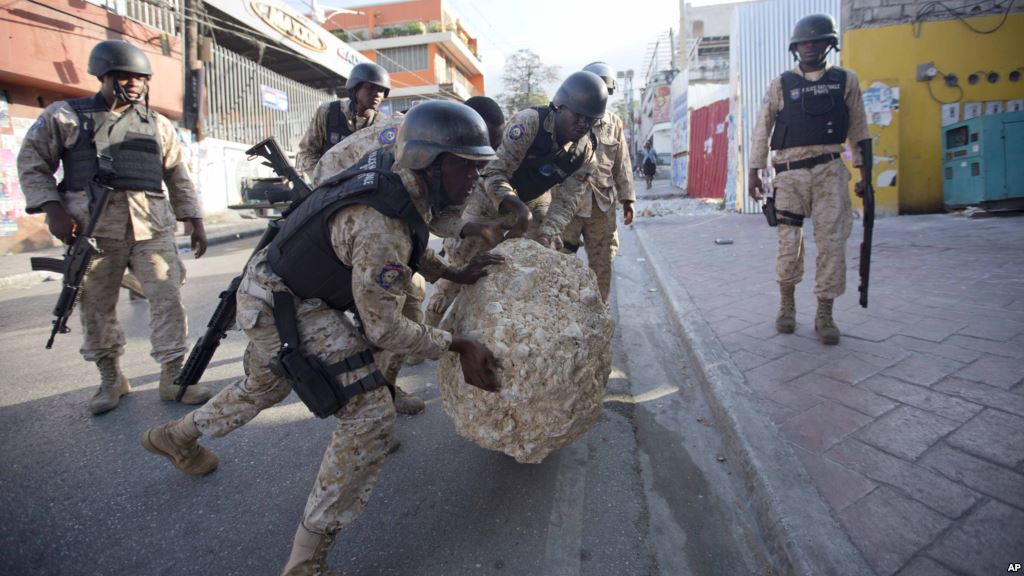 FILE- National police officers remove a rock used as a street barricade by demonstrators after a protest against the results of Oct. 25 elections in Port-au-Prince Haiti on Nov. 18 2015