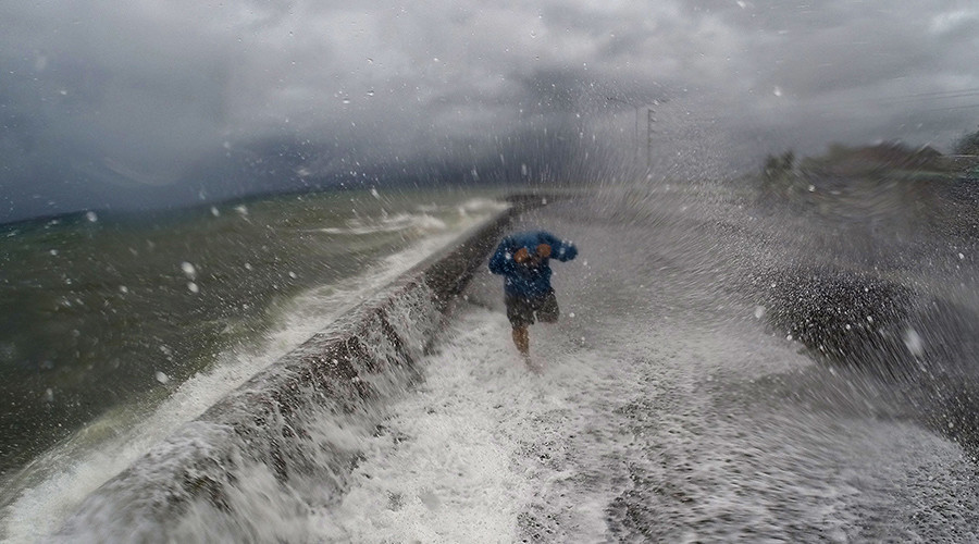 A resident walks past big waves spilling over a wall onto a coastal road in the city of Legaspi in Albay province south of Manila