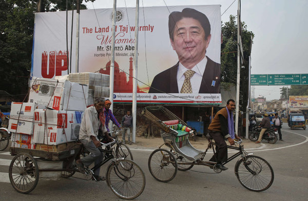 Workers transporting materials in Varanasi India, ride pass a huge poster welcoming Japan´s Prime Minister Shinzo Abe due to arrive this weekend. RAJESH KUMAR SINGH  Associated Press