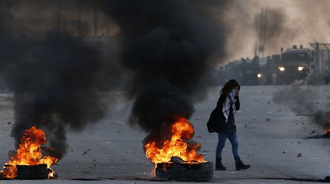 A Palestinian female protester covers her face as she walks past burning tires during clashes with Israeli security forces near the Ofer Israeli military prison located near the West Bank town of Betunia