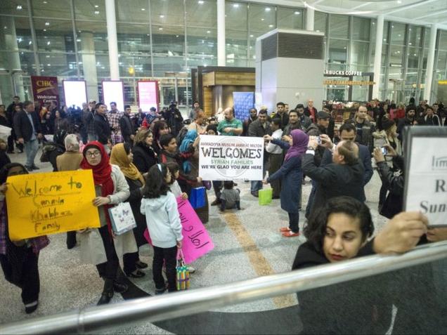 Members of groups who are sponsoring two Syrian refugee families hold up signs welcoming their charges at Toronto Pearson International Airport