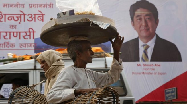 A roadside snack seller passes a poster welcoming Japan's Prime Minister Shinzo Abe in Varanasi India Friday Dec. 11 2015. AFP