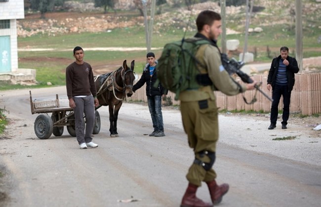 Palestinians wait to be checked by Israeli soldiers patrolling the streets of the West Bank city of Hebron