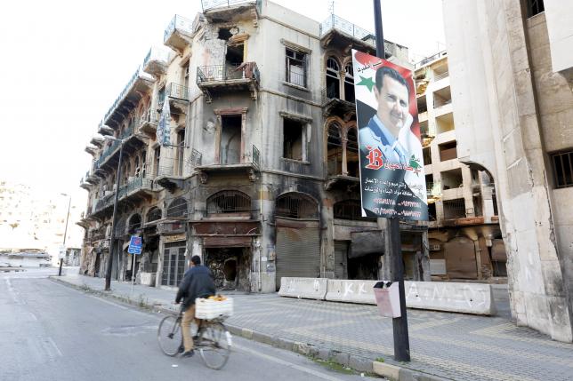 A man rides a bicycle past a poster depicting Syria's President Bashar al Assad near the new clock square in the old city of Homs Syria