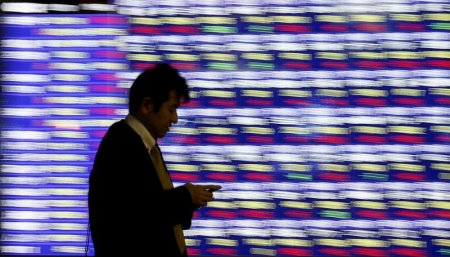 A man holding a mobile phone walks past an electronic stock quotation board outside a brokerage in Tokyo Japan