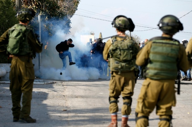 A Palestinian protester takes cover from tear gas smoke during clashes with Israeli soldiers