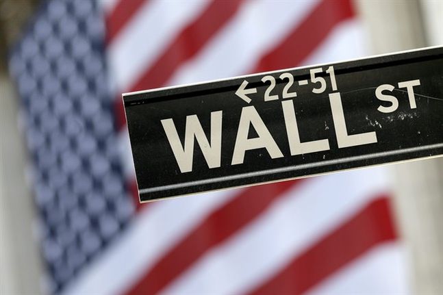 Wall Street street sign is framed by a giant American flag hanging on the facade of the New York Stock Exchange. Global shares were mixed in trading Wednesday Dec. 30 2015 with only some markets che