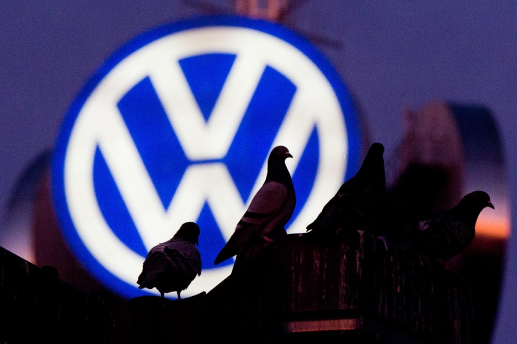 Pigeons sit on a street lantern in front of the illuminated logo of German car maker Volkswagen