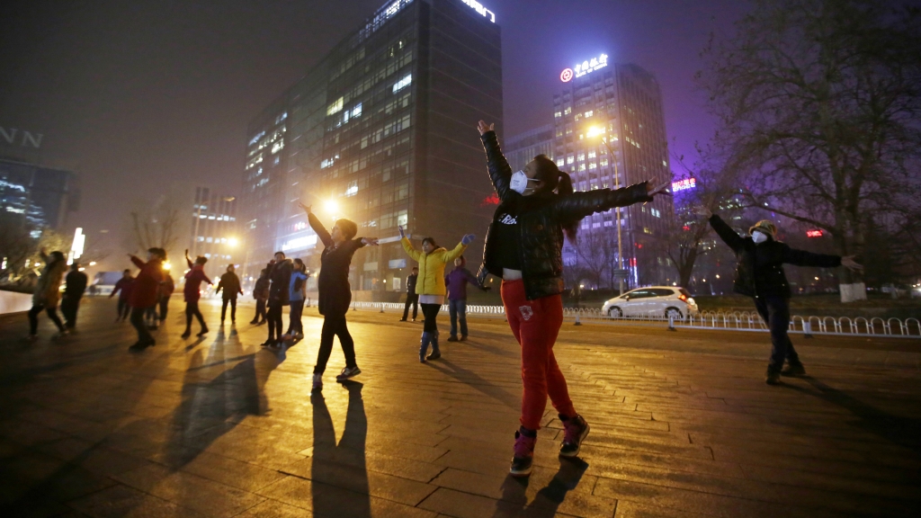 Women wearing masks and other residents dance during their daily exercise amid the heavy smog in Beijing on Monday