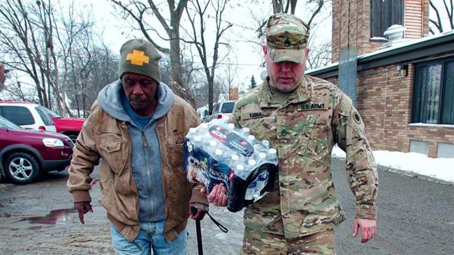 A Michigan National Guard Staff Sergeant helps a Flint resident take bottled water out to his car