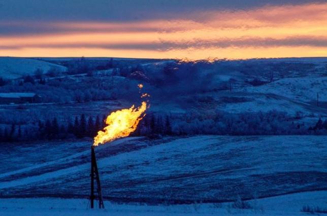 A natural gas flare on an oil well pad burns as the sun sets outside Watford City North Dakota