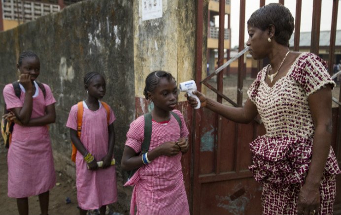 A woman uses an infrared thermometer to take the temperature of girls as they arrive at Coleyah Centre Primary School in Conakry the capital