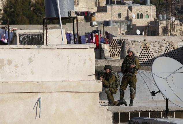 An Israeli soldier aims his weapon at Palestinians as Israeli settlers take over several houses which are disputed between Palestinians and Israelis in the West Bank old city of Hebr