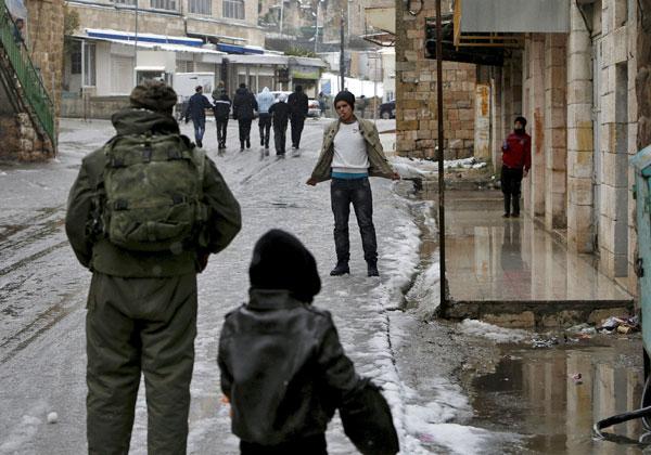 An Israeli soldier inspects a Palestinian during a snowstorm in the West Bank city of Hebron on Tuesday