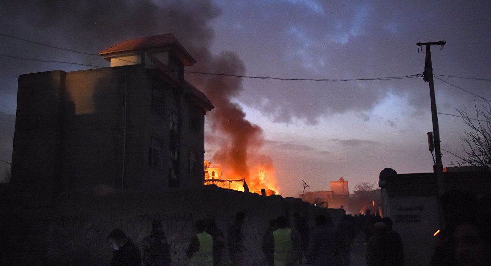 Security personnel and bystanders look on as flames and smoke rise at the site of a suicide car bomb attack at a French restaurant Le Jardin in Kabul