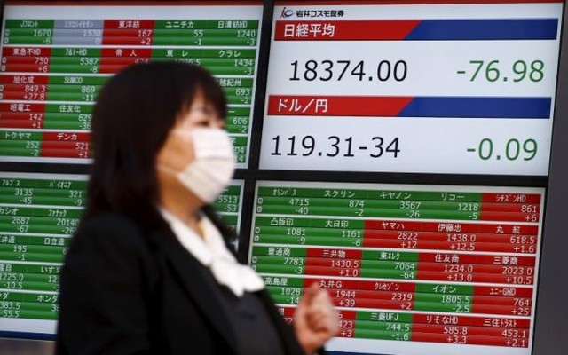 A woman walks past a screen displaying market data and exchange rates between the Japanese yen and the U.S. dollar outside a brokerage in Tokyo Japan