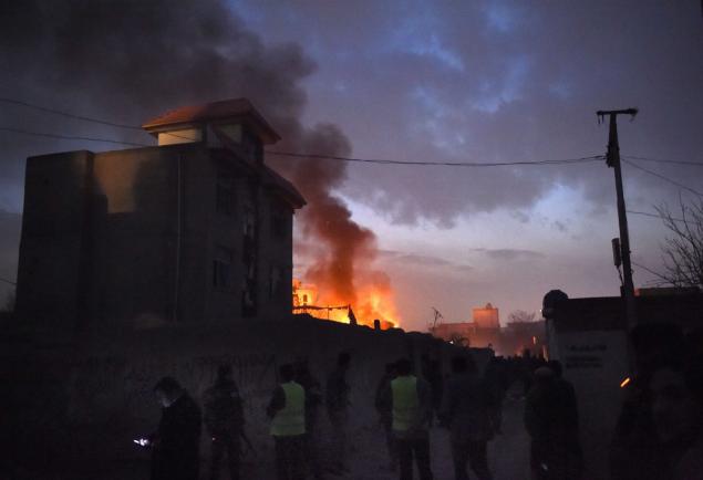 Security personnel and bystanders look on as flames and smoke rise at the site of a suicide car bomb attack at a French restaurant on Friday