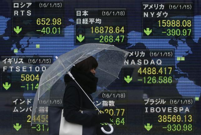 A pedestrian holding an umbrella walks past at an electronic board showing the stock market indices of various countries outside a brokerage in Tokyo Japan