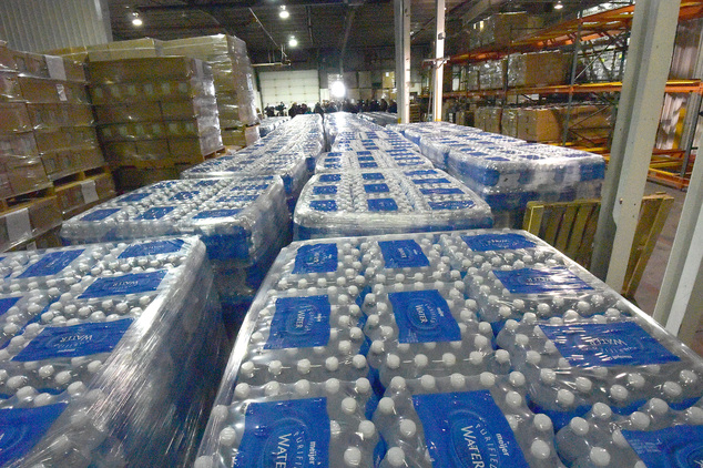 Thousands of bottles of water await distribution in a county warehouse as volunteers accompanied by Michigan State Police and Gennessee County Sheriff's Depu