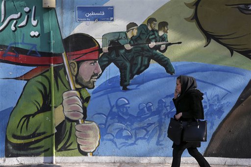 An Iranian woman walks past a mural depicting Iranian armed forces in the battlefield at Palestine Sq. in Tehran Iran Saturday Jan. 16 2016. The end of Western sanctions against Iran loomed Saturday as Iran's foreign minister suggested the U.N