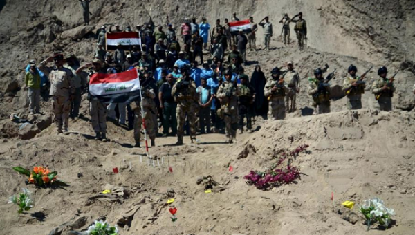 Iraqi soldiers salute as they stand next to a mass grave for Shi