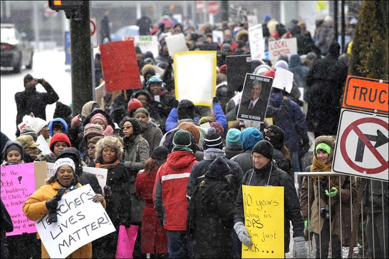 Burton International Academy computer advanced teacher Denice McGee bottom left holds a sign as she and other protesters wait to cross the street Wednesday Jan. 20 in Detroit