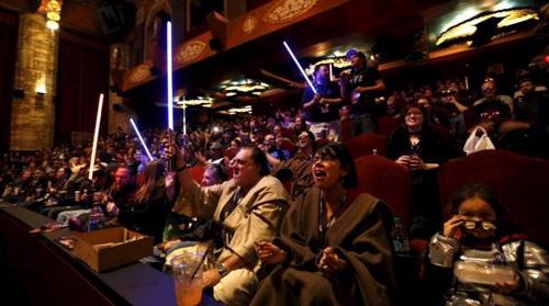 Moviegoers cheer and wave lightsabers before the first showing of the movie