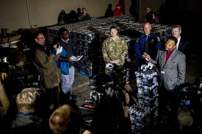 Cameras and reporters surround Flint Fire Chief David Cox who speaks into microphones atop stacks of bottled water during a press conference on Wednesday Jan. 13 2016 announcing the arrival of seven Michigan National Guard soldiers to help aid at Flin