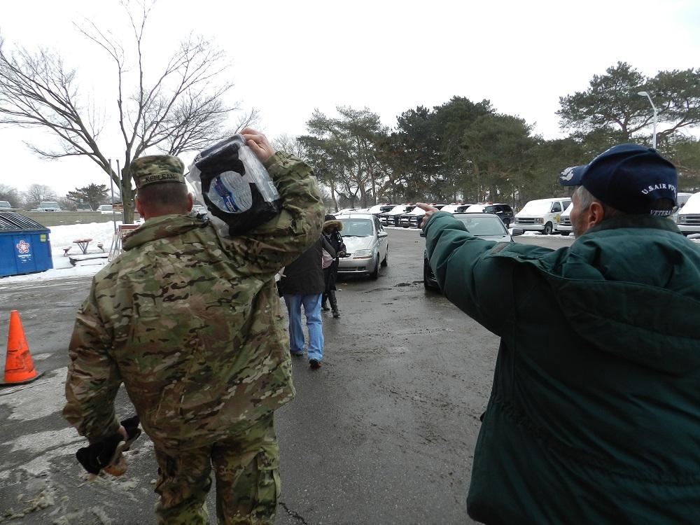 Major John Keelean carries a case of bottled water for a Flint man for the pick up entrance at Flint Fire Station #1