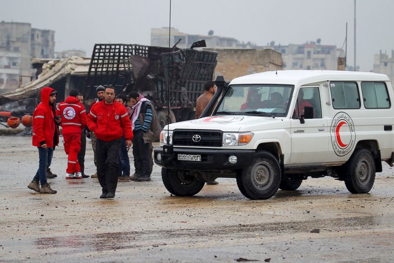 Red Crescent workers stand near their vehicles prior to inspection from rebels before heading to al Foua and Kefraya in Idlib province Syria