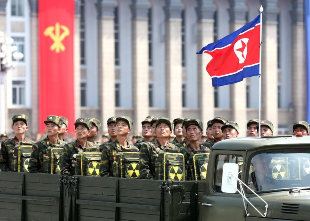 North Korean soldiers turn and look towards leader Kim Jong Un as they carry packs marked with the nuclear symbol during a parade